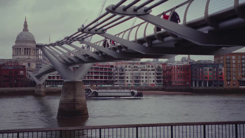 Ferry crosses under bridge busy with pedestrians with domed historic building in the background