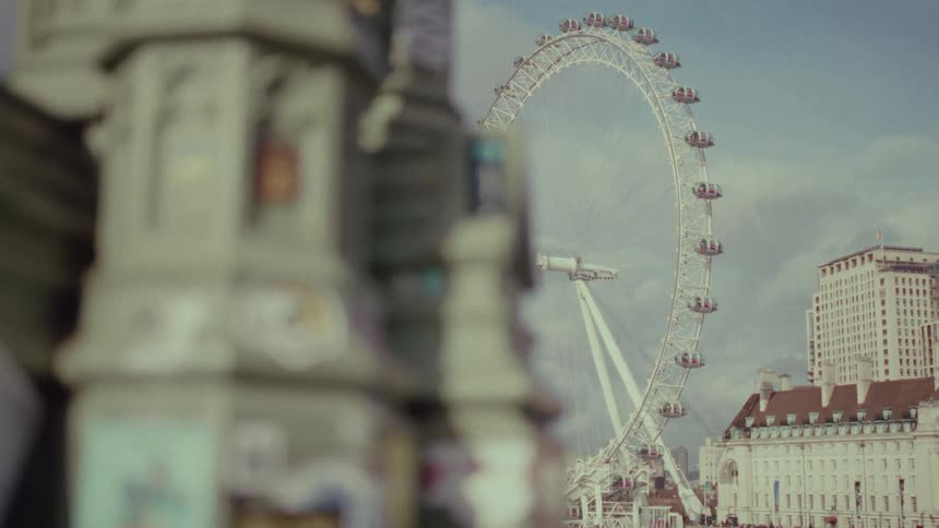 A ferris wheel in a city behind a structure with a piece of paper falling down through the cracks