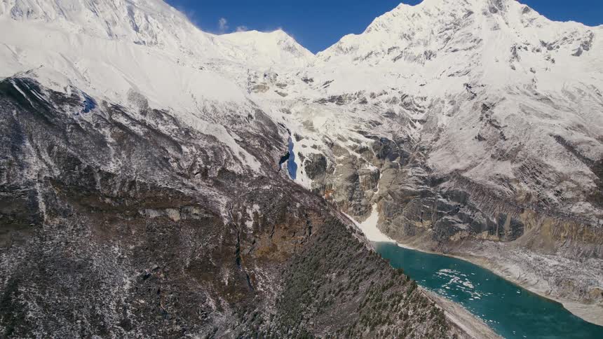 Snow covers tops of mountains while vegetation covers lower slopes near lake