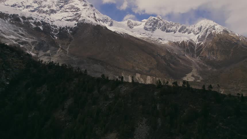 A mountain range with snow at the top a few trees and a valley with a lake