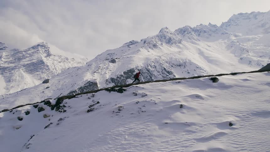 A lone hiker makes their way along a snow covered mountain ridge