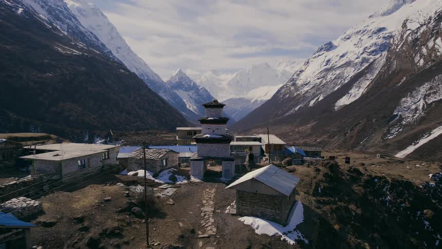 A campsite with small buildings and tents at the base of a large mountain range