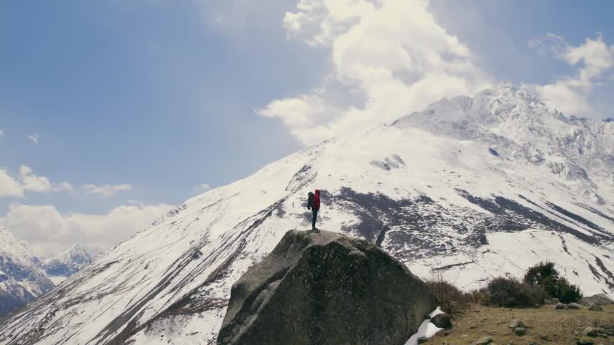Backpacker stands on rock formation with view of mountains and nearby fortress
