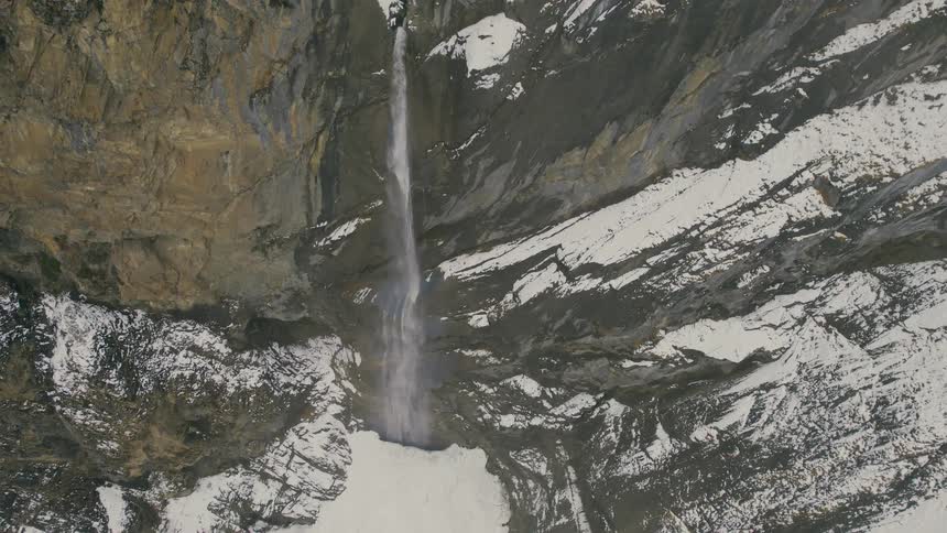 A waterfall falls down a cliff on a mountain with snow