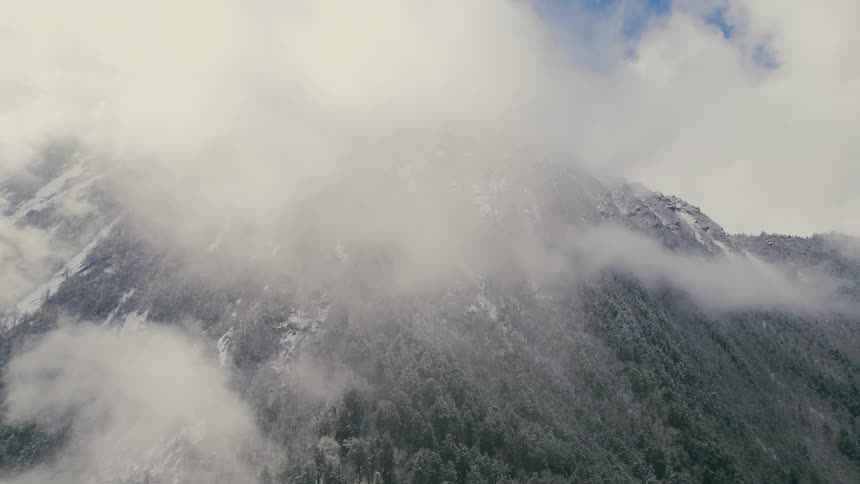 Aerial view of forested mountain slope surrounded by clouds