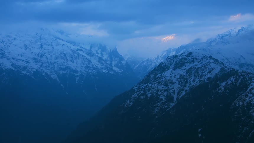 Snow covered mountains stand tall under a cloudy sky at dusk