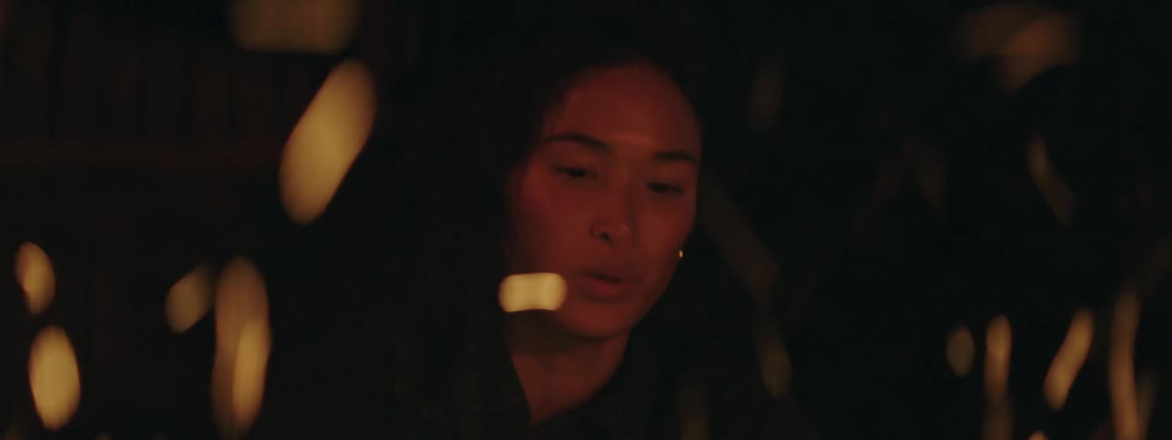 The fire is burning at night as a woman drinks and one talks