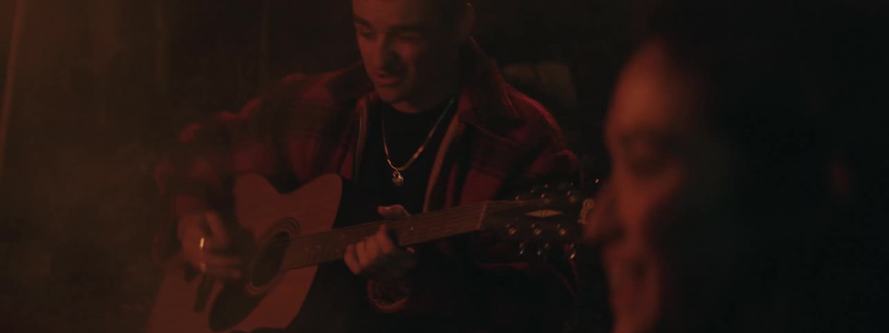 A woman smiles as she listens to a man sing and play guitar
