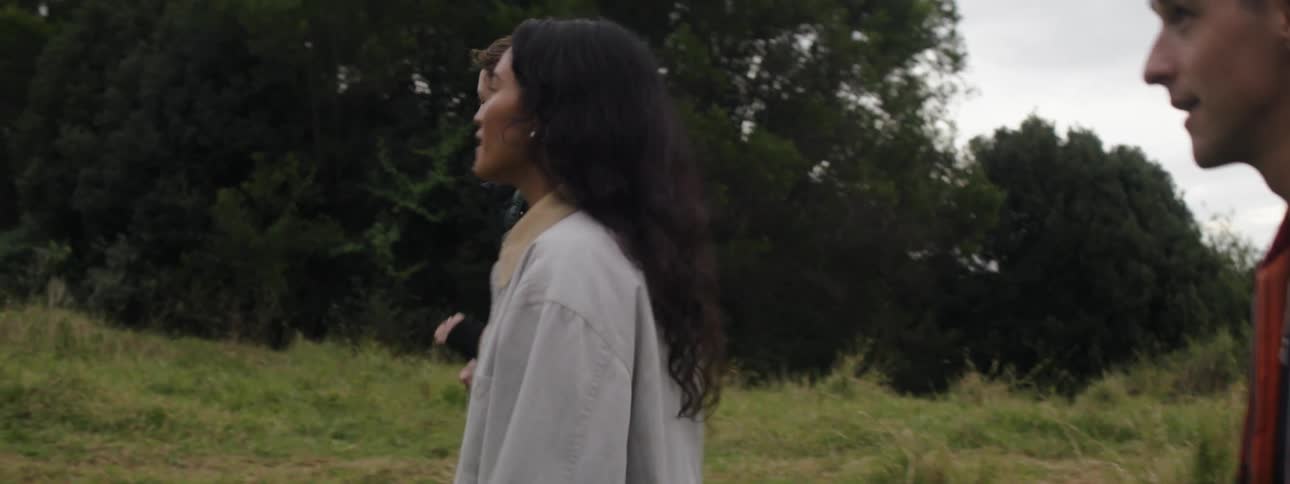 A teenage girl walks in a grassland with two teenage boys