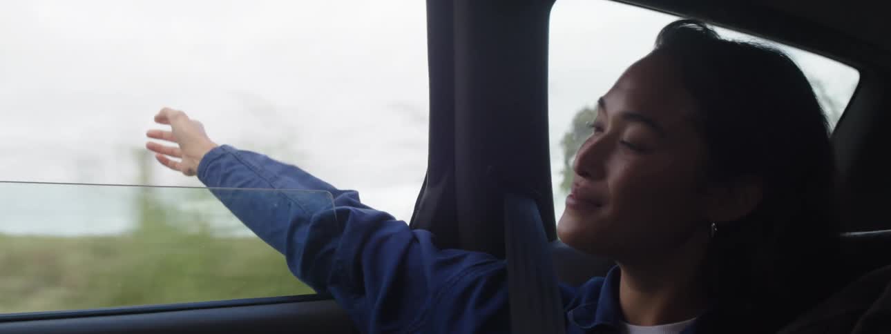 A joyful woman inside a car stretching her hands outside while laughing and smiling clearly enjoying the journey to the fullest