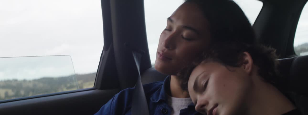 Female passengers sleep against each other while traveling through countryside