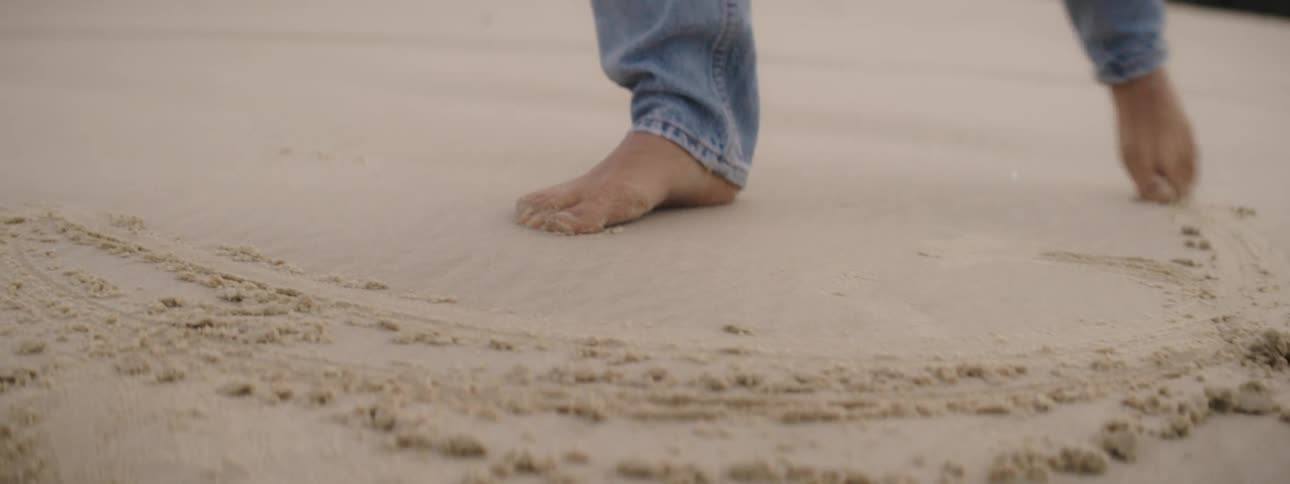 Woman wearing jeans draws a circle using her feet on the beach