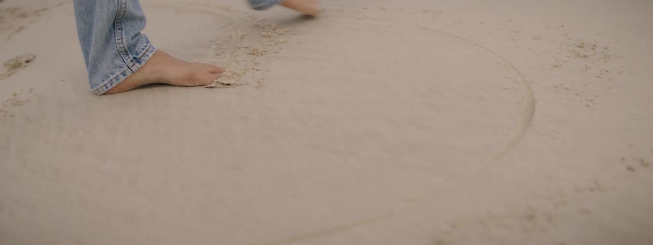A person is drawing with their bare feet in the sand