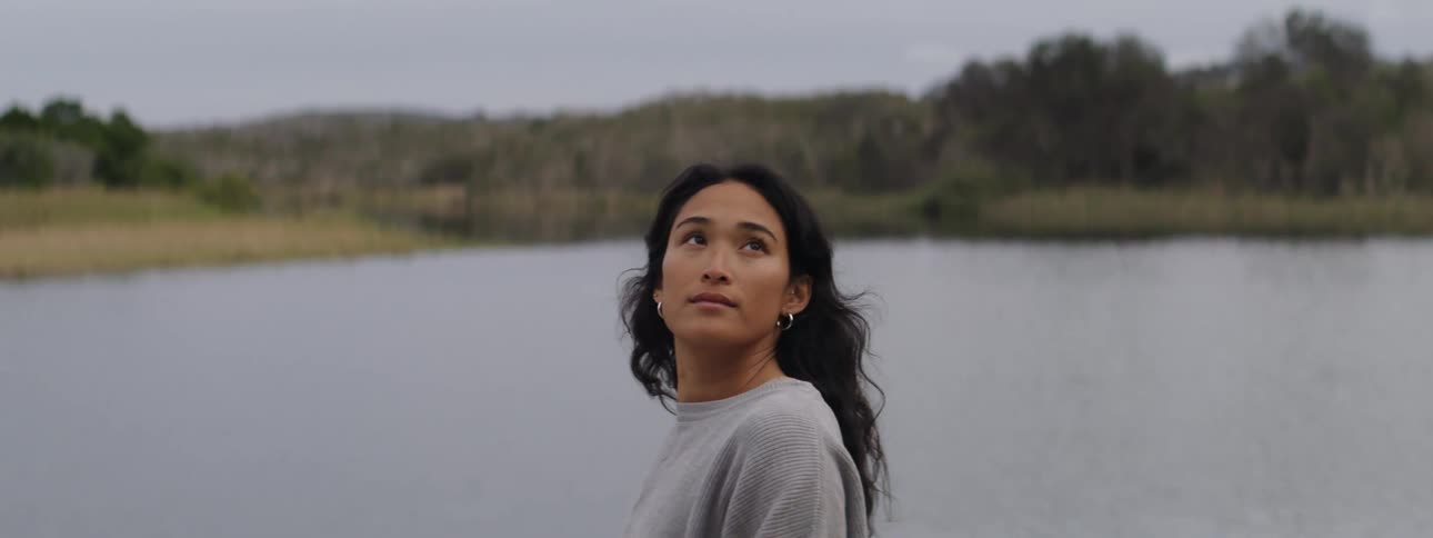 Woman stands on lake shore across from hills and looks around