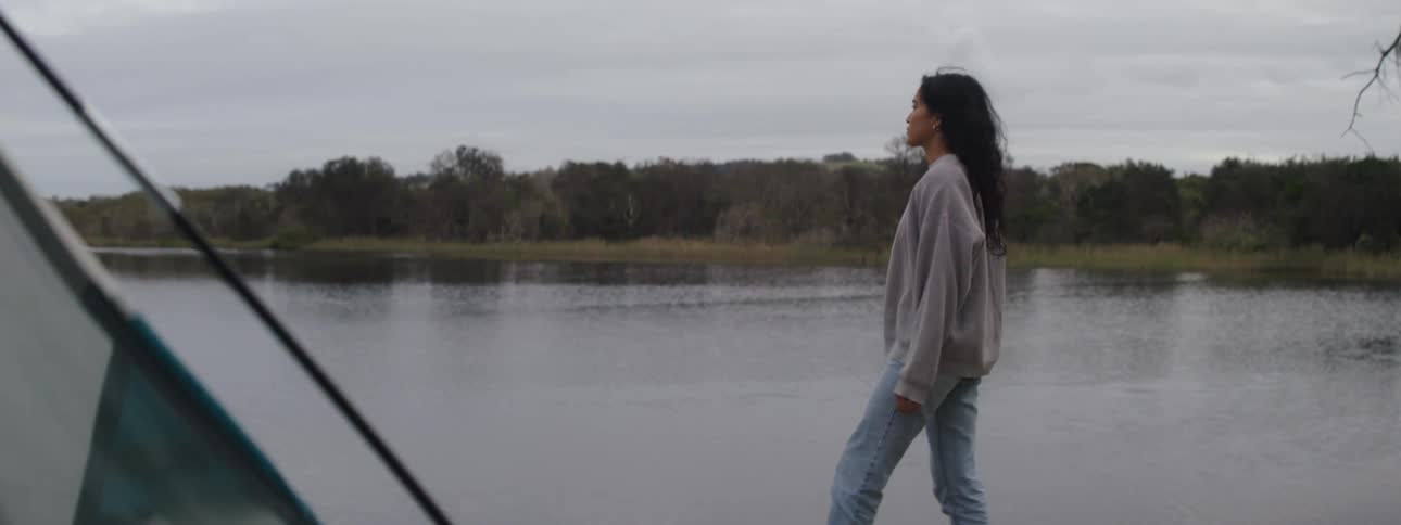A young woman stretches and walks back and forth near a river
