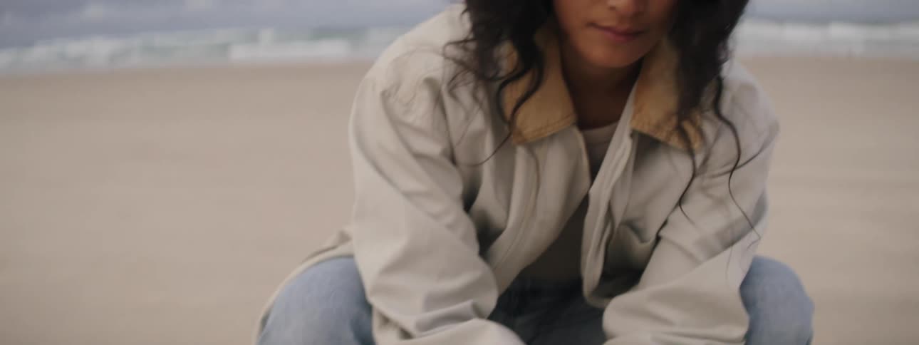 A woman crouches down and holds sand in her hands while at the beach