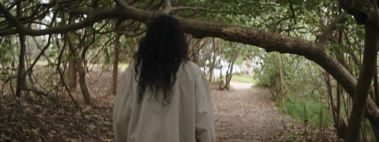 A woman with long curly hair walks along a trail in a forest