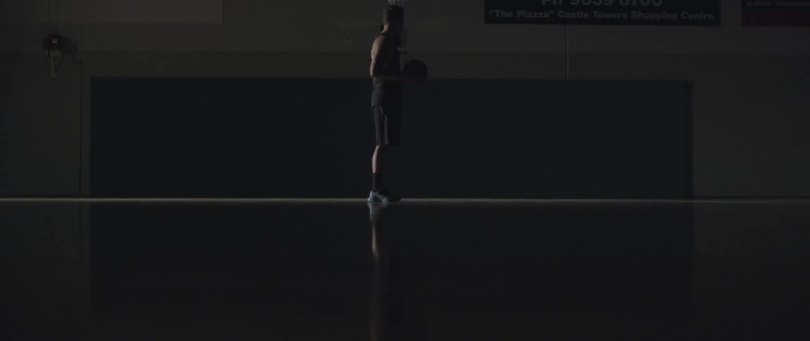 A man holds a basketball in a dark gymnasium