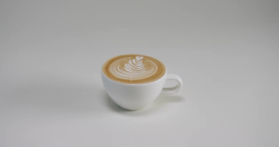 A small white cup has a caffeinated beverage in it with cream