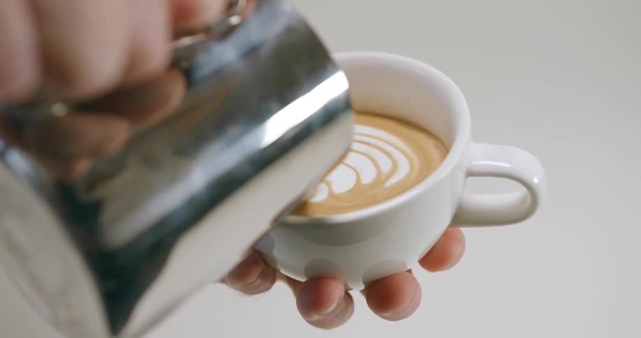 A person holds a small cup while pouring cream into a caffeinated beverage
