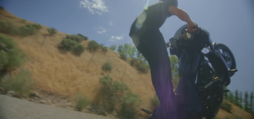 A man doing motorcycle stunts down a country road as someone else watches them