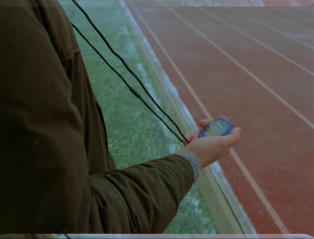A man at a running track holding a stop watch