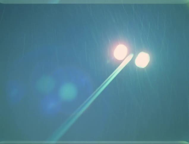 At nighttime and as snow falls a tall pole has two brightly shining lights atop it