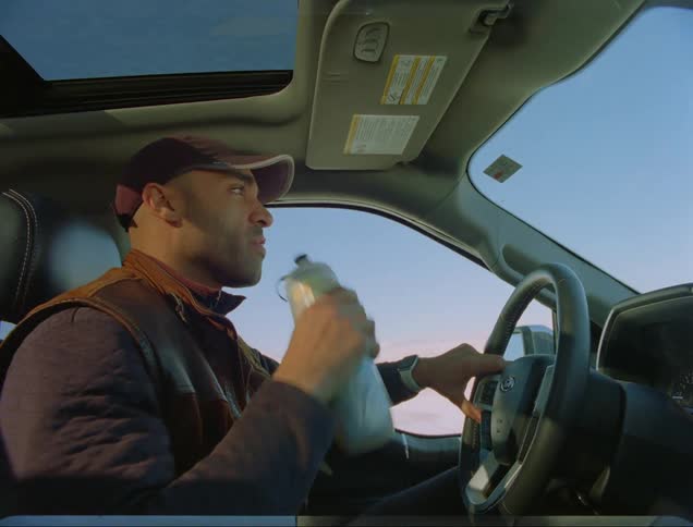A man drinks from a water bottle while driving a vehicle during the day