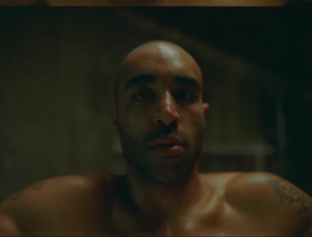 A man sitting in a tin bathtub filled with ice stares into the camera
