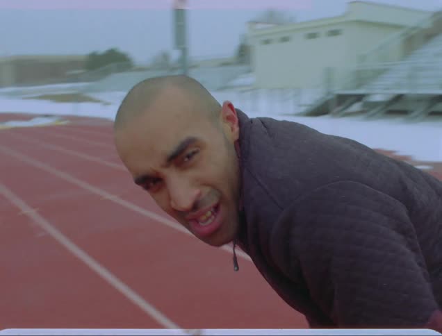 Man bends to catch his breath on running track near now covered field and stands