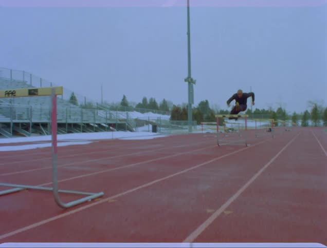 A man runs fast and jumps over hurdles lines up on a track
