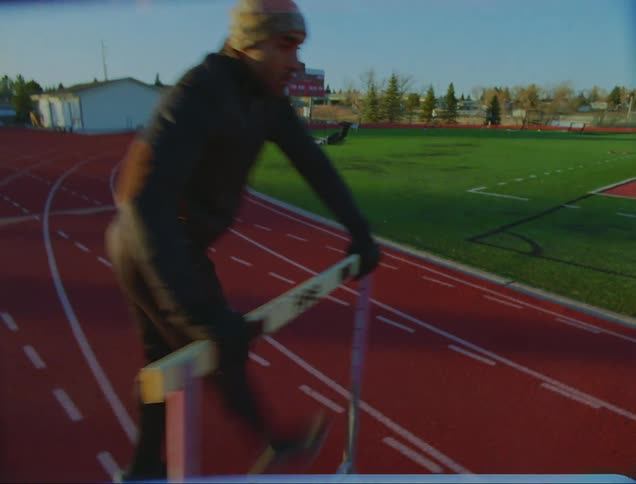A young man on a track swings his legs to the side as he warms up