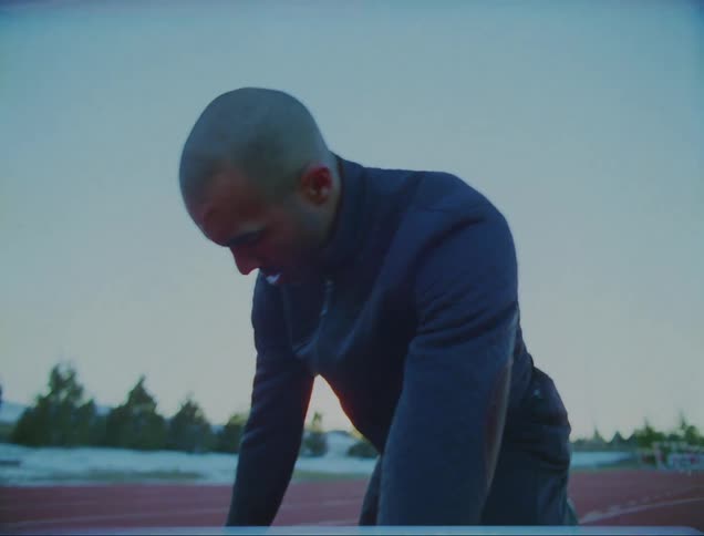 A man on a track jumps to warm up and then puts his feet in starting blocks and runs