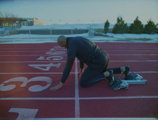 A man on a track jumps down and gets into position on starting blocks and takes off and runs