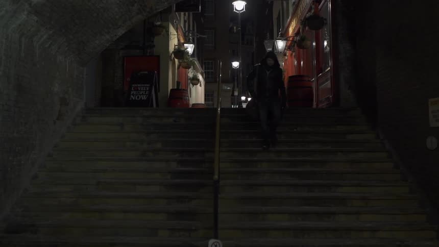 Man in trench coat walking down stairs in a town