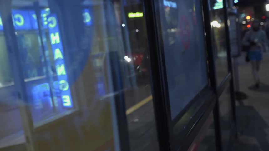 A hooded person walks down a city street at night