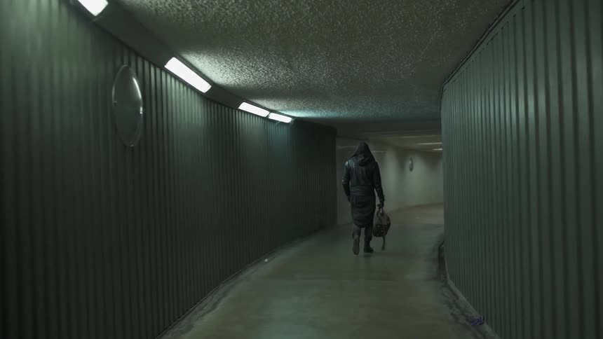 A man is carrying a bag and walking down a narrow tunnel