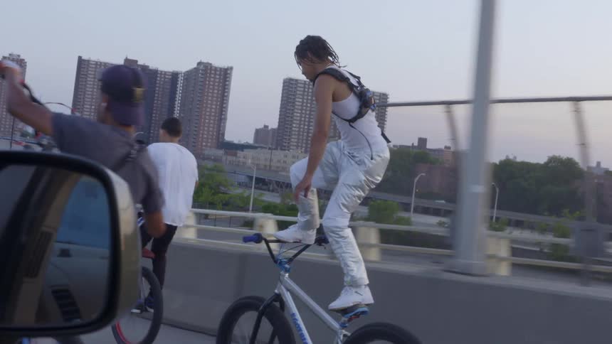 A group of young men perform daring tricks on their bicycles while on the road