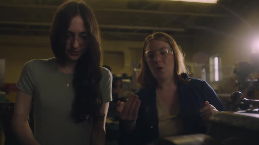 A woman is teaching a younger woman how to use a machine in a factory