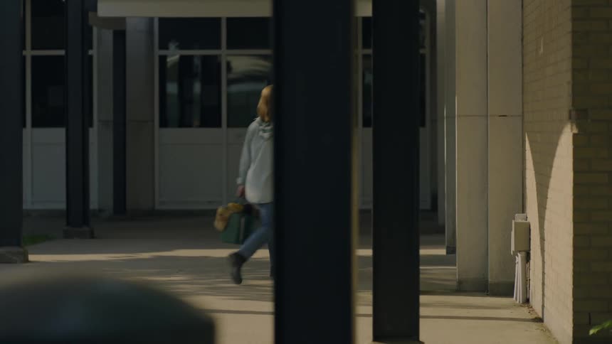 A woman walks briskly towards a building and enters the door