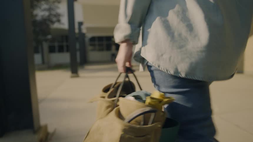 A person carrying a hand bag walks on the campus at morning