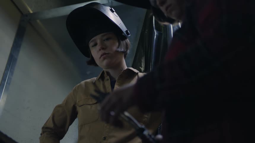 Two women in a welding workshop as one teach the other one how to handle welding equipment