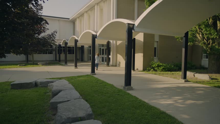 A woman carrying a bag walks briskly towards the entrance of a large building