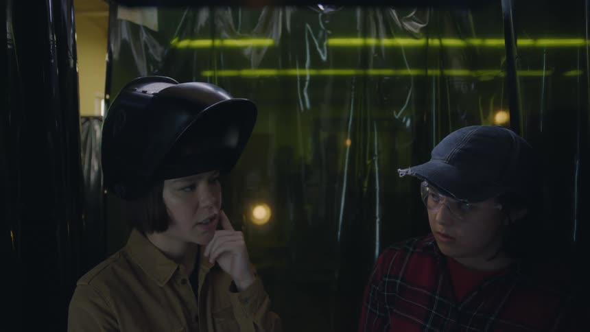 Two students wearing protective gear talk to each other in the workshop