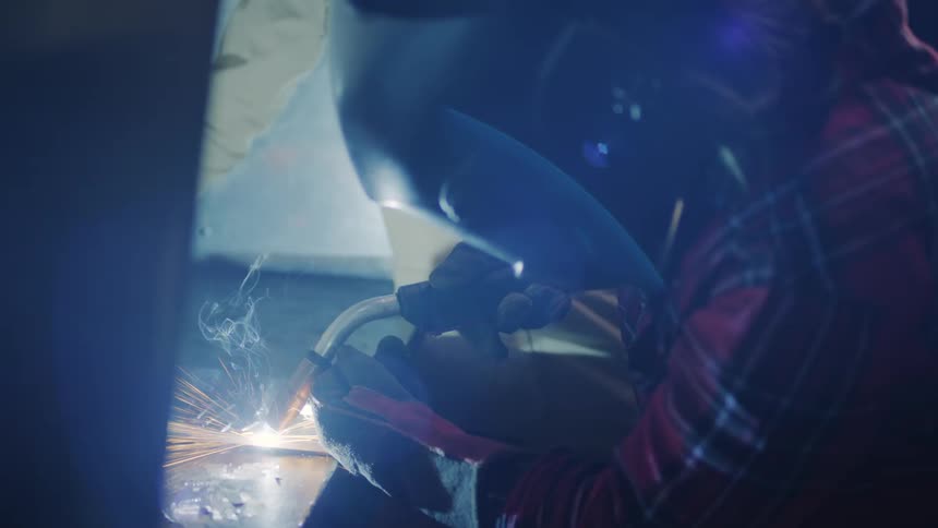 One women welds a piece of metal while another stands nearby observing