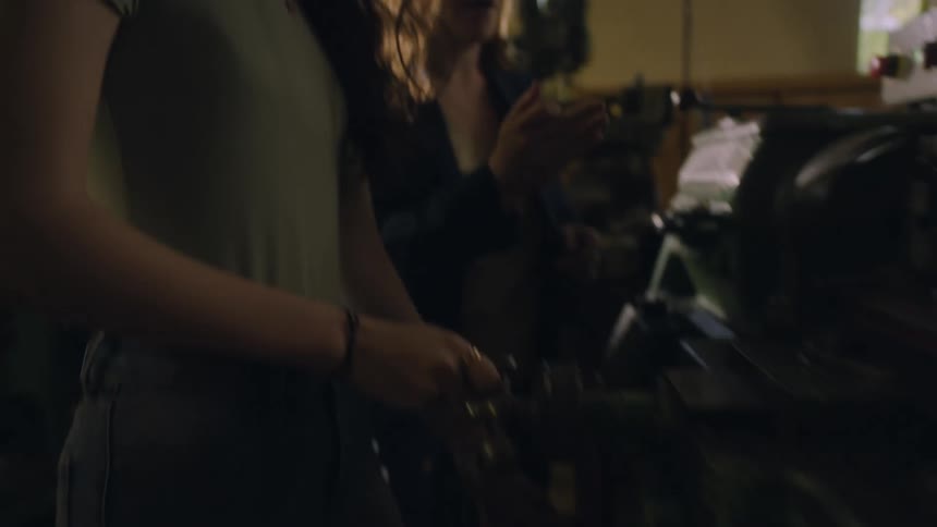 Older woman wearing protective goggles teaching a younger woman how to operate a machine indoors