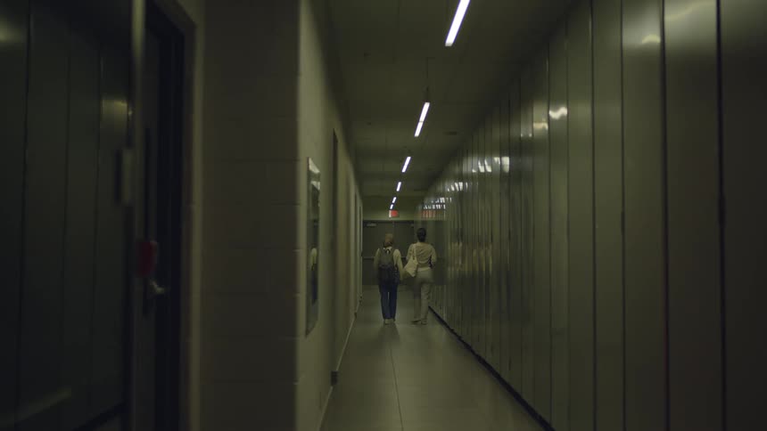 Two women walk together down a long and narrow hallway