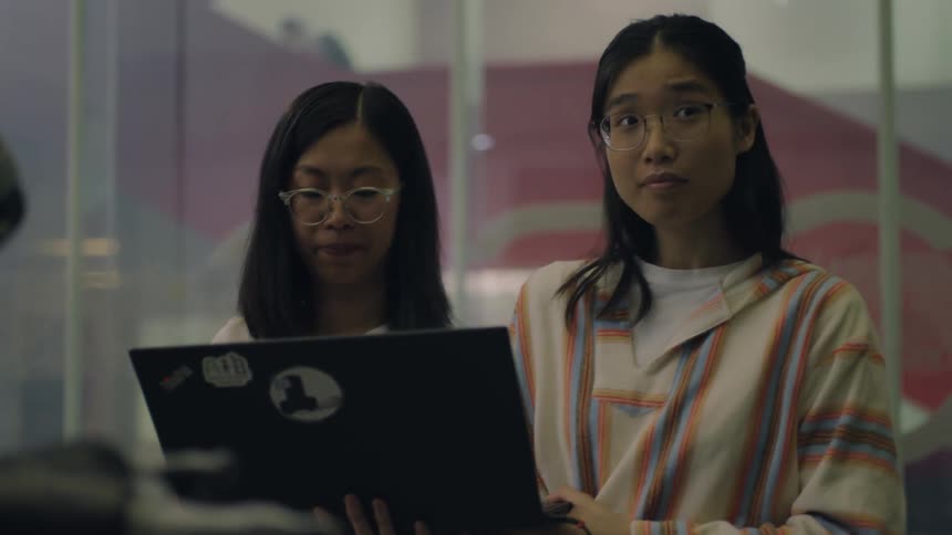 Two students holding a laptop work near a robot in the university