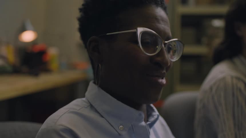 Smiling shorthaired woman wearing classy glasses talks to friends sitting in a room