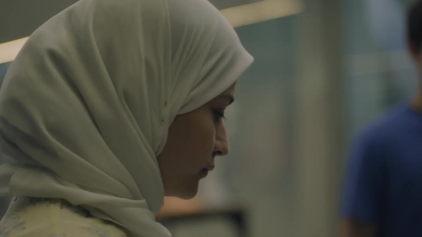 A young woman concentrates while a young man stands nearby in a laboratory